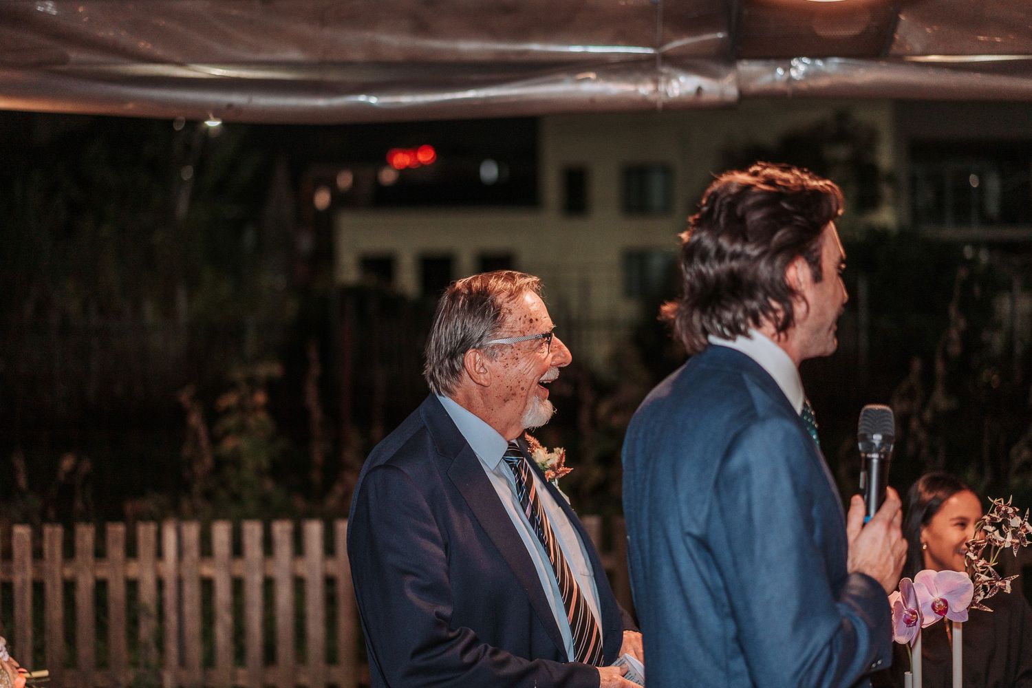 People gathered outdoors at night during a wedding reception with ambient lighting and floral decorations.