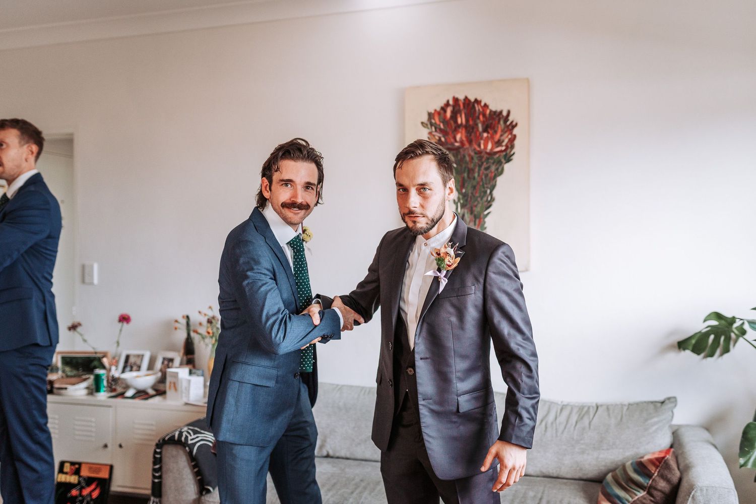 Two men in fitted suits shake hands while smiling in a bright room with white walls and modern decor.