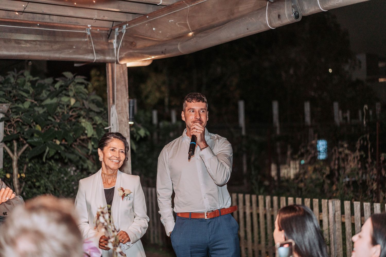 People enjoying an evening outdoors under wooden beams during a social gathering or celebration.