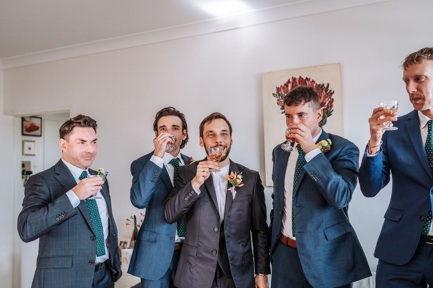 Wedding party members in blue suits share drinks together during pre-ceremony preparations.