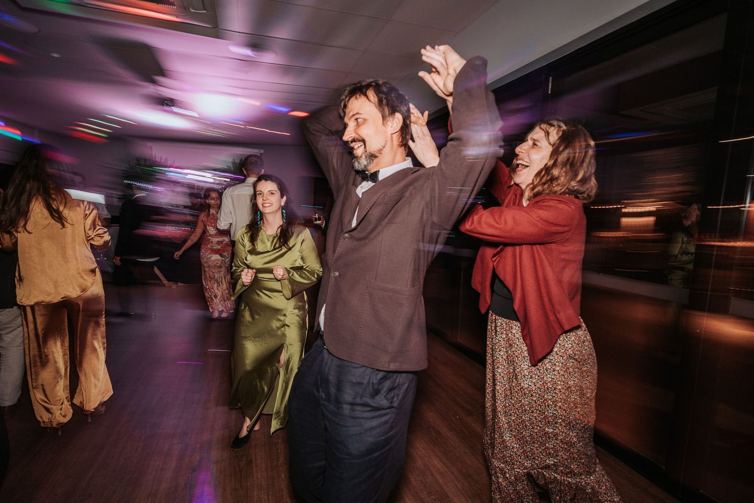 People dancing enthusiastically at a party with motion blur and colorful lighting effects in a dark venue.