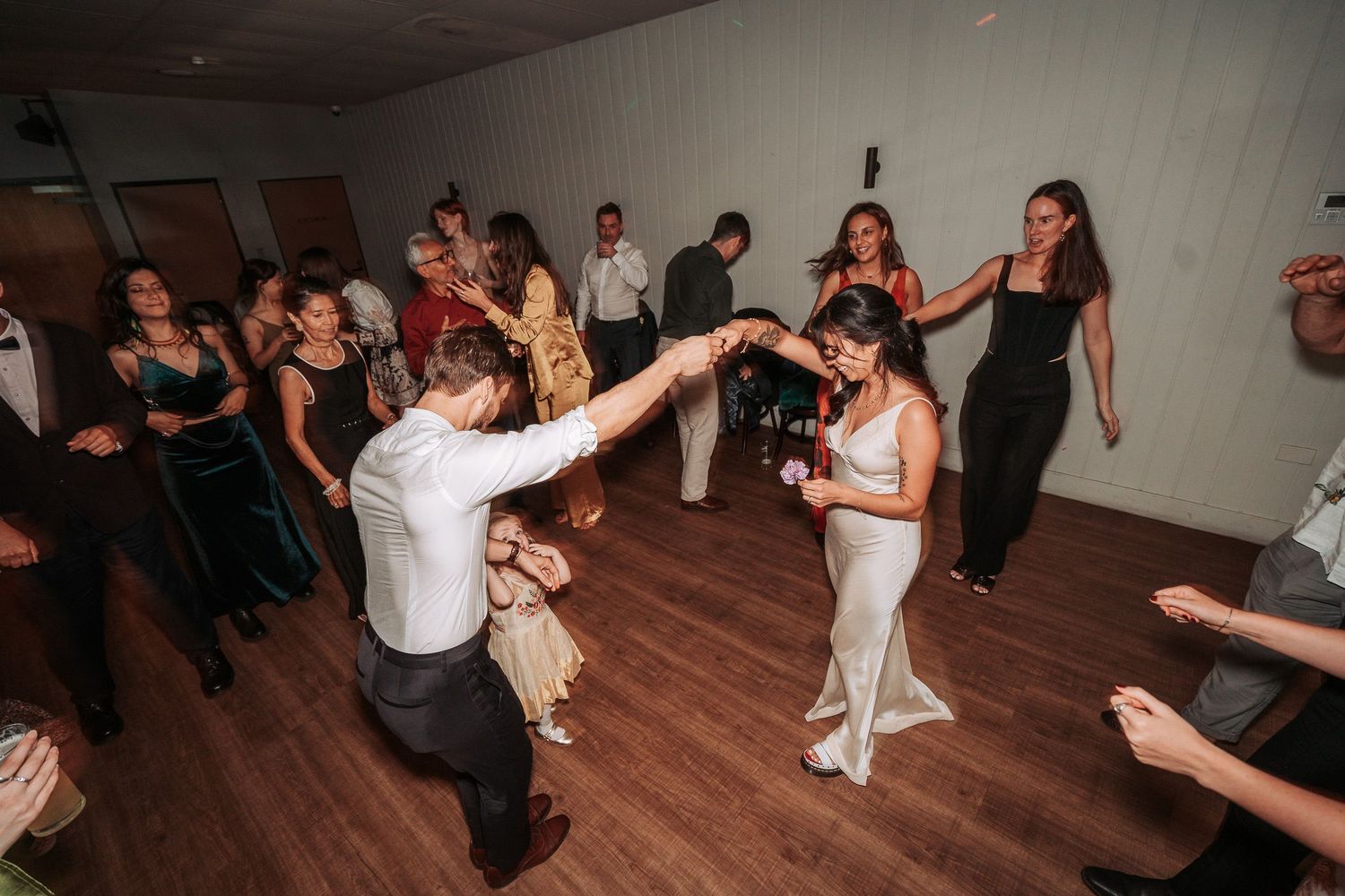 People dancing and celebrating on a wooden dance floor at a festive indoor event with white walls.