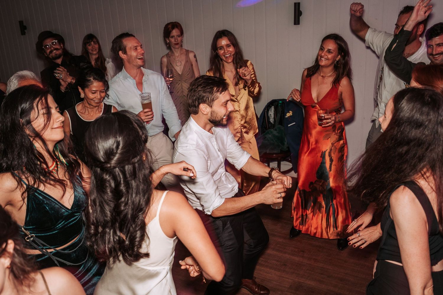 Party guests in formal attire dancing and enjoying themselves on a wooden dance floor at a celebratory event.