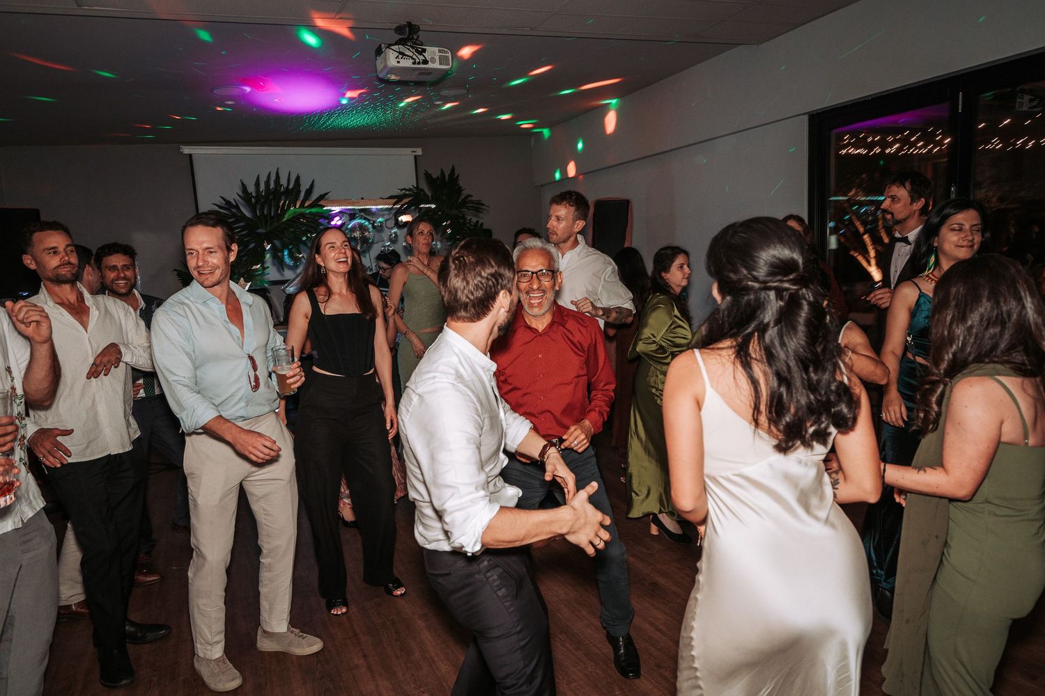 People dancing at a reception party with disco lights illuminating the dance floor.