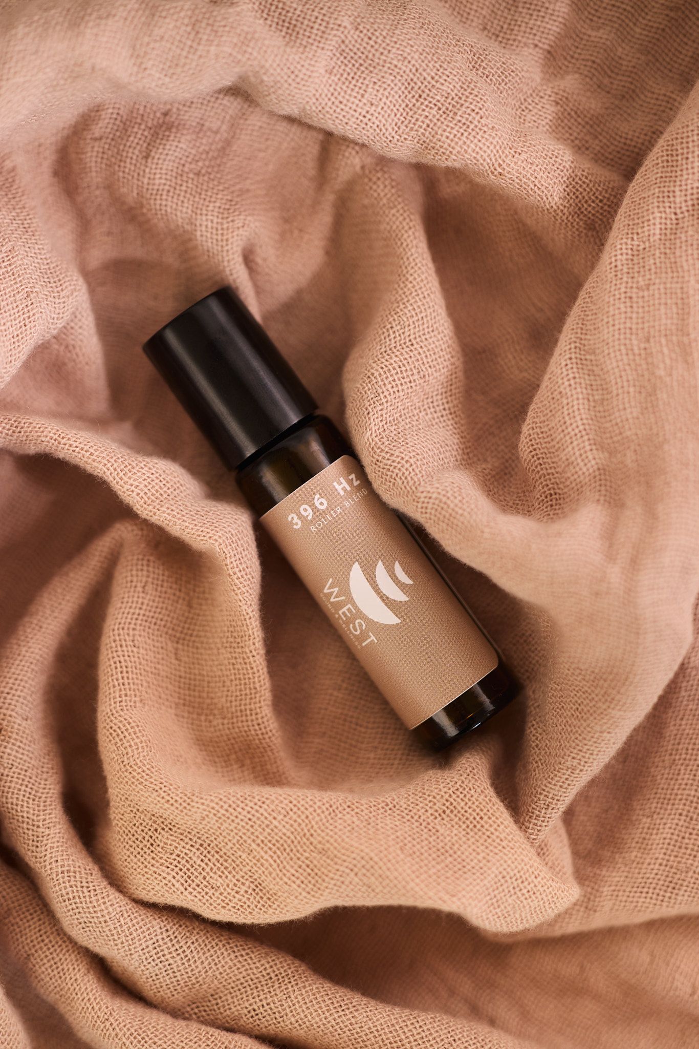 A brown cosmetic bottle lying on textured beige linen fabric with soft natural lighting and folds creating shadow detail.