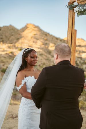 Couple shares emotional moment during wedding ceremony with desert mountains in background.
