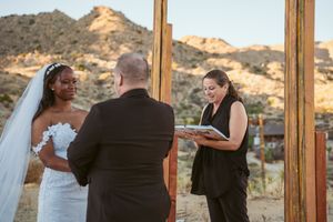 Wedding ceremony takes place outdoors in a desert landscape with mountains glowing in golden sunset light.