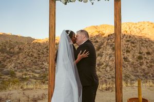 Romantic desert wedding ceremony at sunset with a wooden arch and mountainous backdrop.