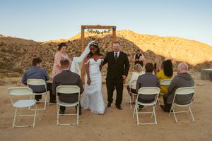Small outdoor wedding ceremony taking place in a desert landscape with mountains at sunset.