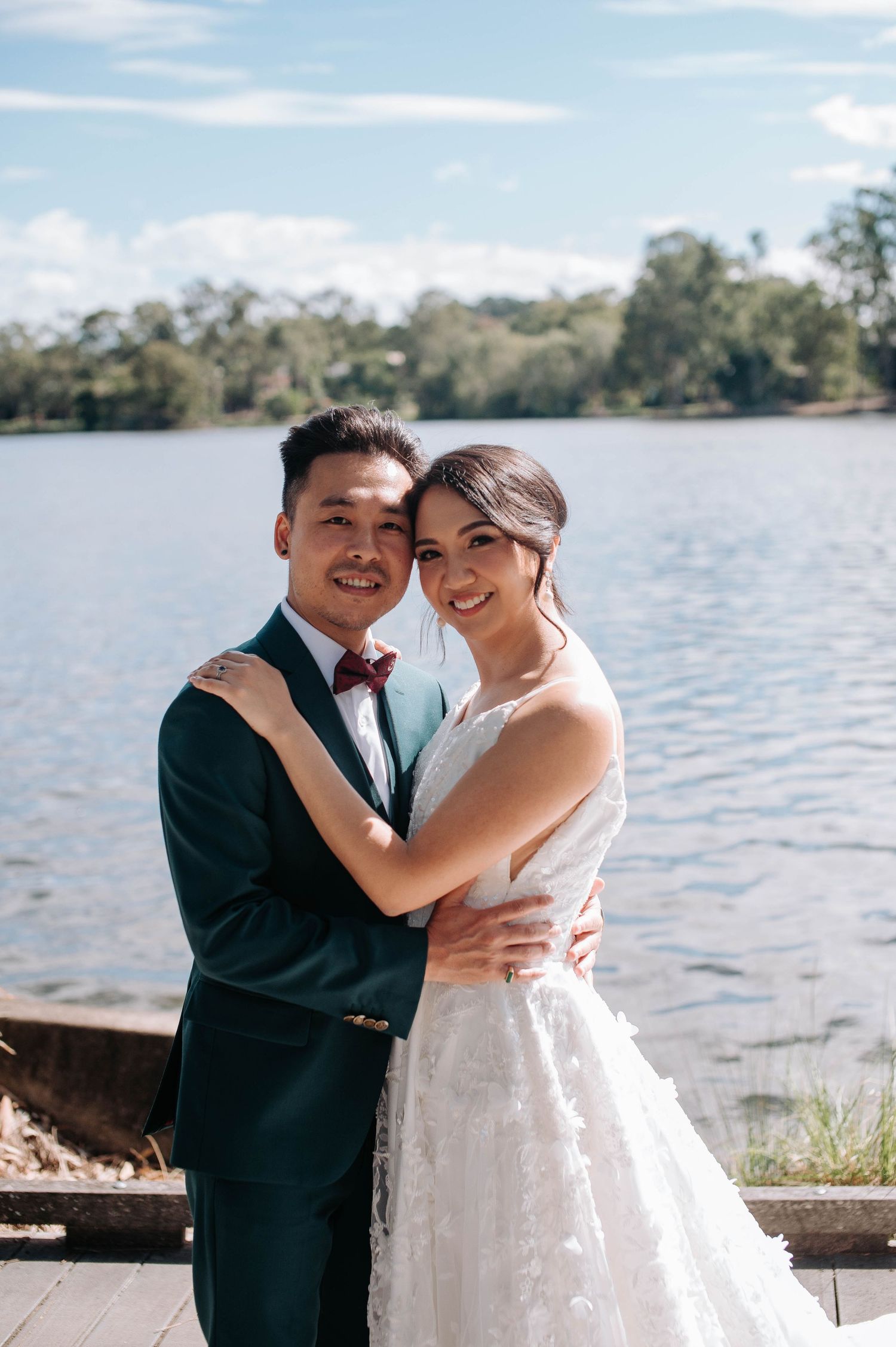 A bride and groom pose together on a dock overlooking a serene lake on their wedding day.