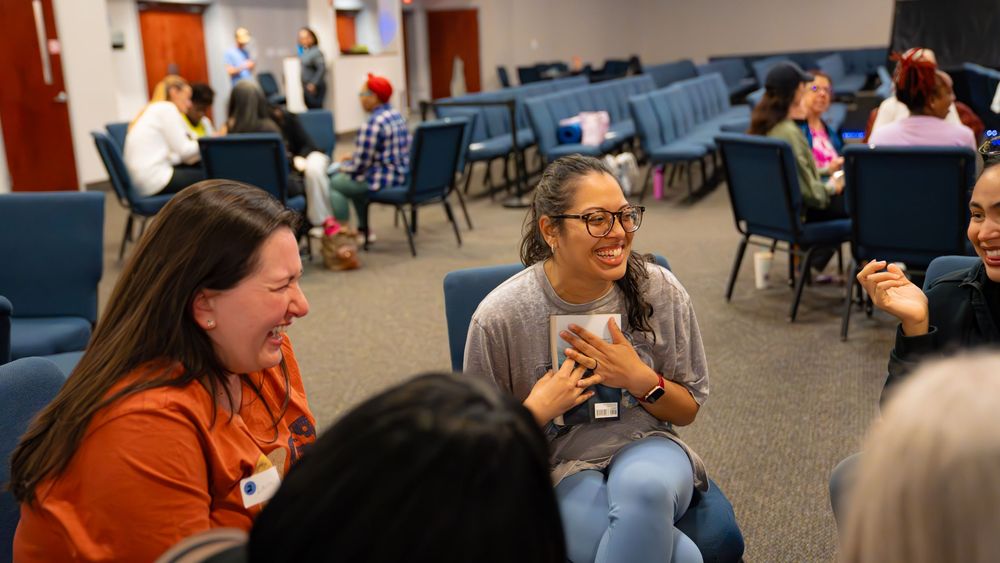 People share laughter and conversation while seated in a meeting room with blue chairs.