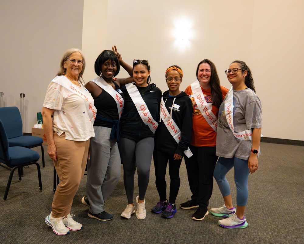 A group poses together wearing sashes for a celebratory photo in an indoor venue.
