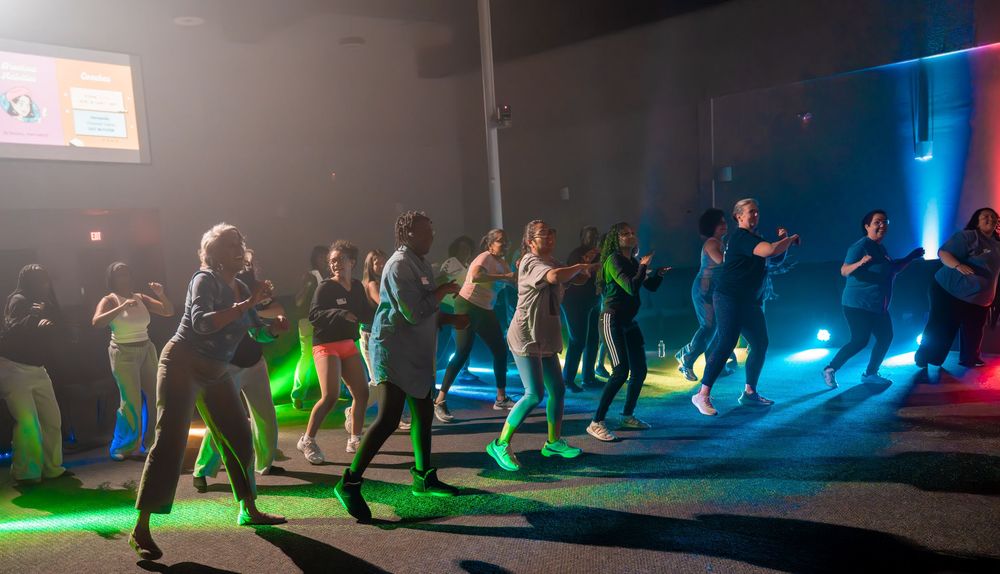 A group dances together under colorful lighting effects in a dark room.