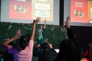 Audience members raise their hands during a presentation with projected slides.