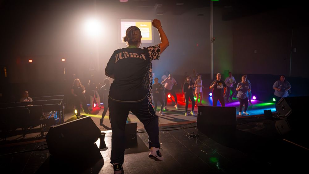 A performer on stage raises their arm while entertaining a crowd in a darkened venue.