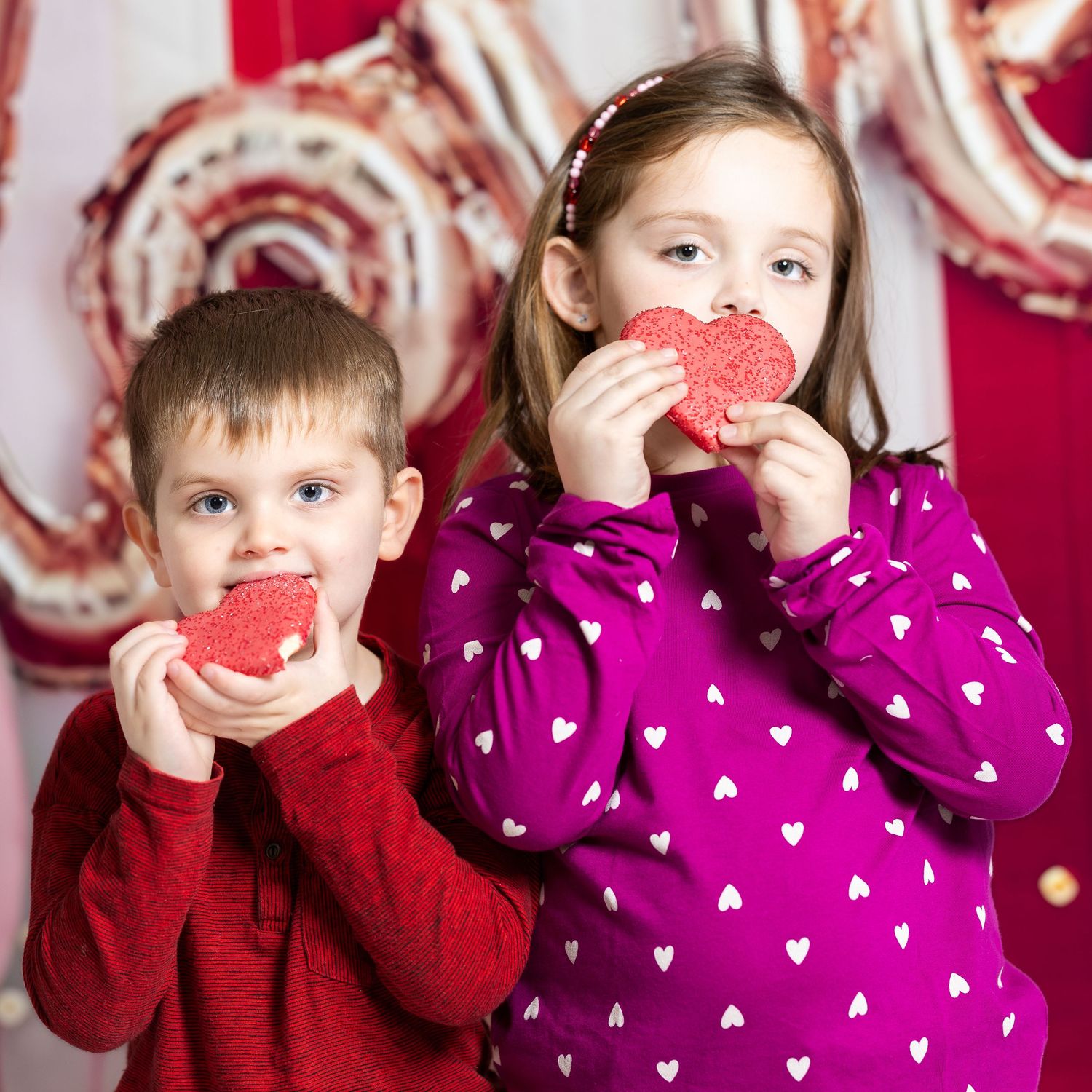 Child wearing a white and pink patterned sweater with a heart-shaped hair accessory against a blurred background.