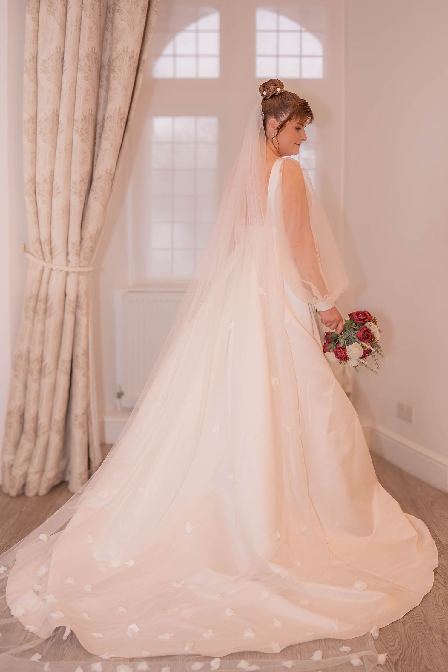 Flowing white wedding dress with cathedral-length train photographed in elegant room with natural light.