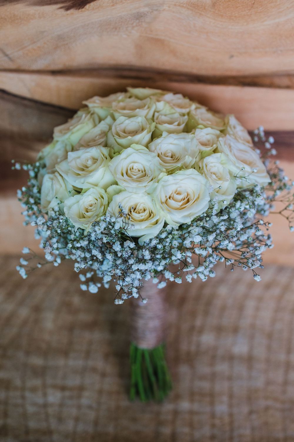 A beautiful wedding bouquet featuring white roses surrounded by delicate baby's breath flowers on a rustic wood background.