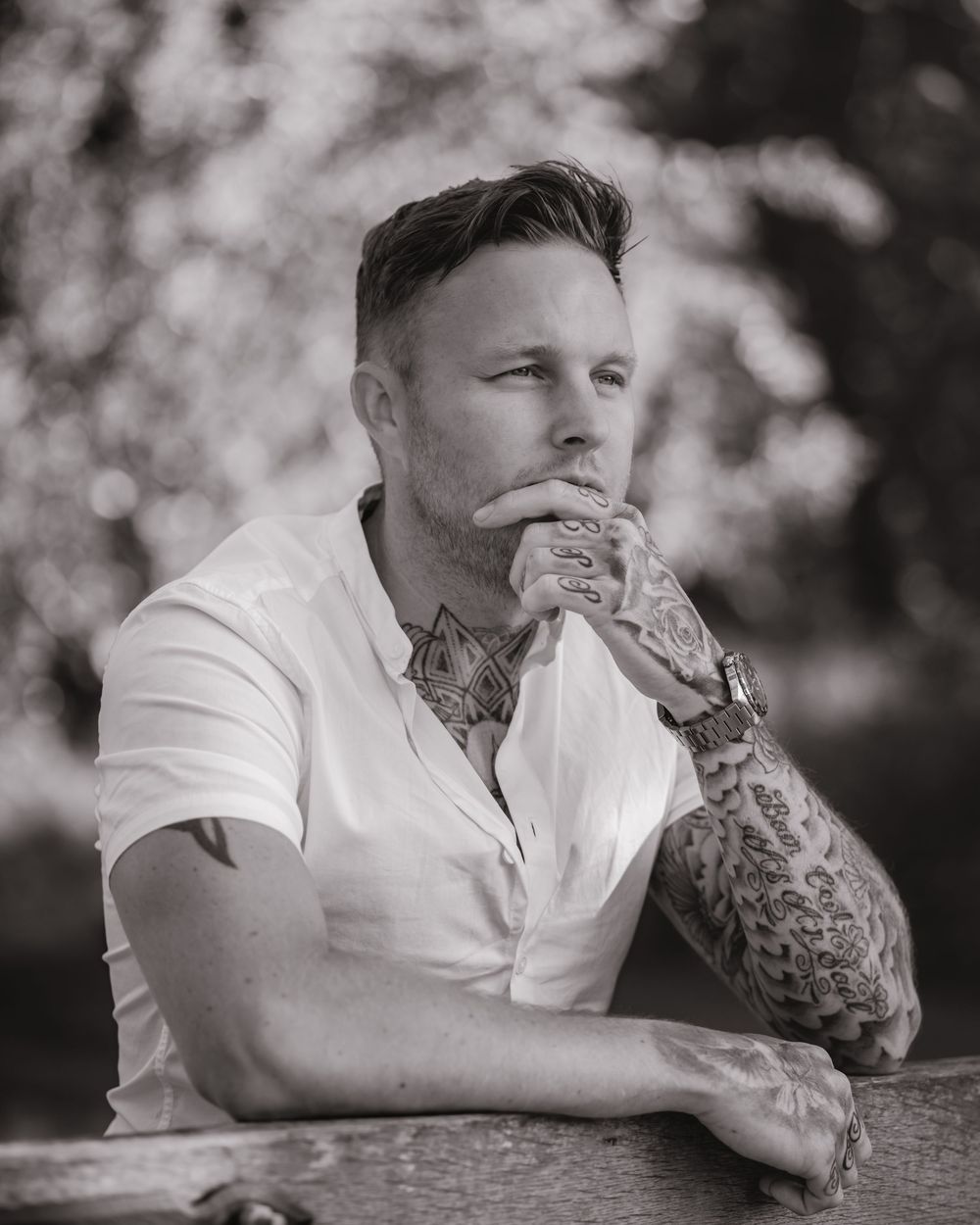 Black and white portrait showing person in white shirt with detailed arm tattoos.