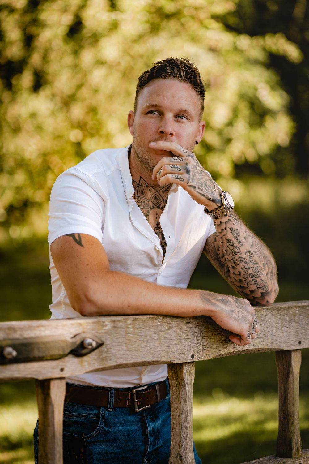 Outdoor portrait showing person with intricate sleeve tattoos leaning on wooden fence.