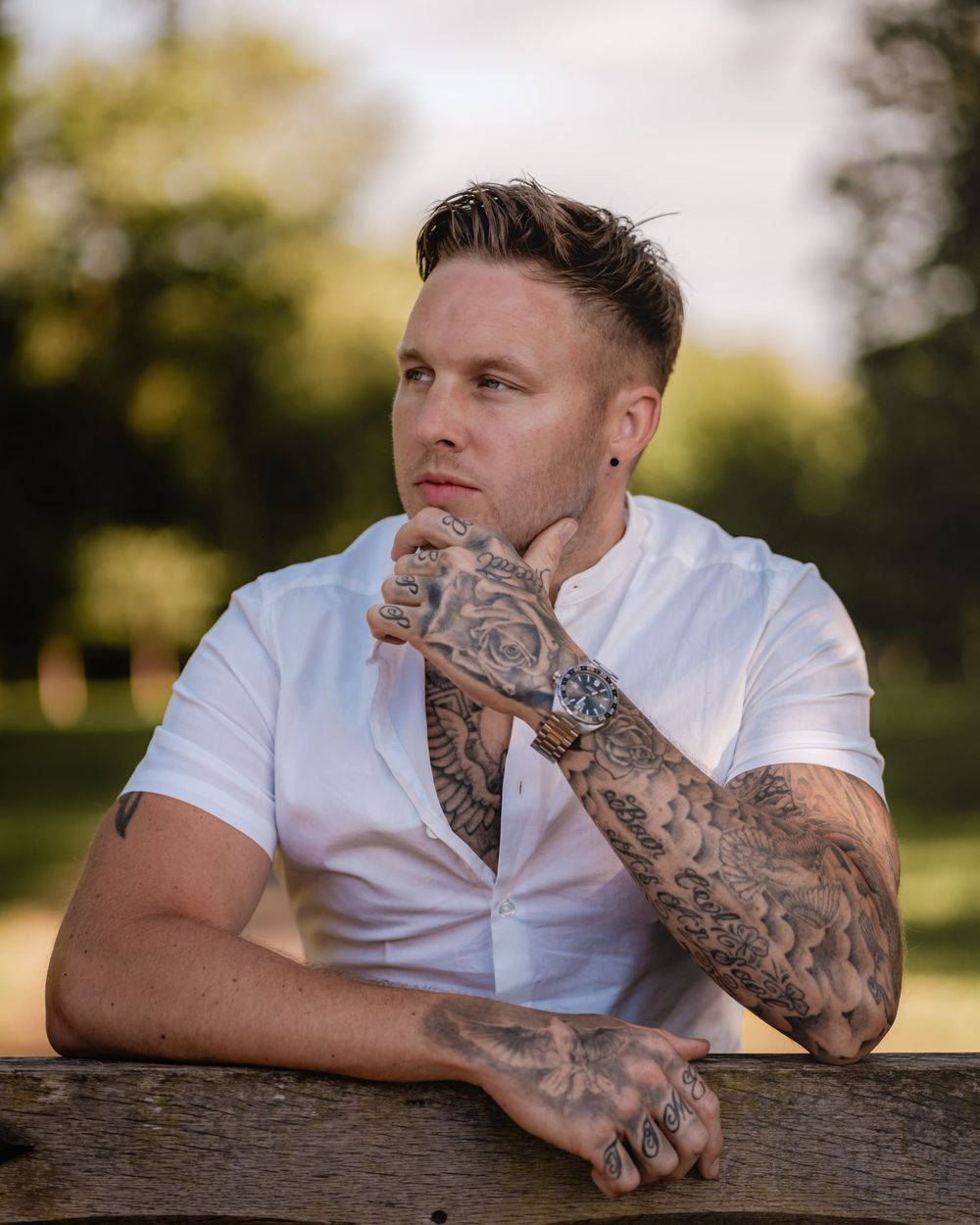 Casual outdoor portrait featuring white shirt and detailed sleeve tattoo artwork.
