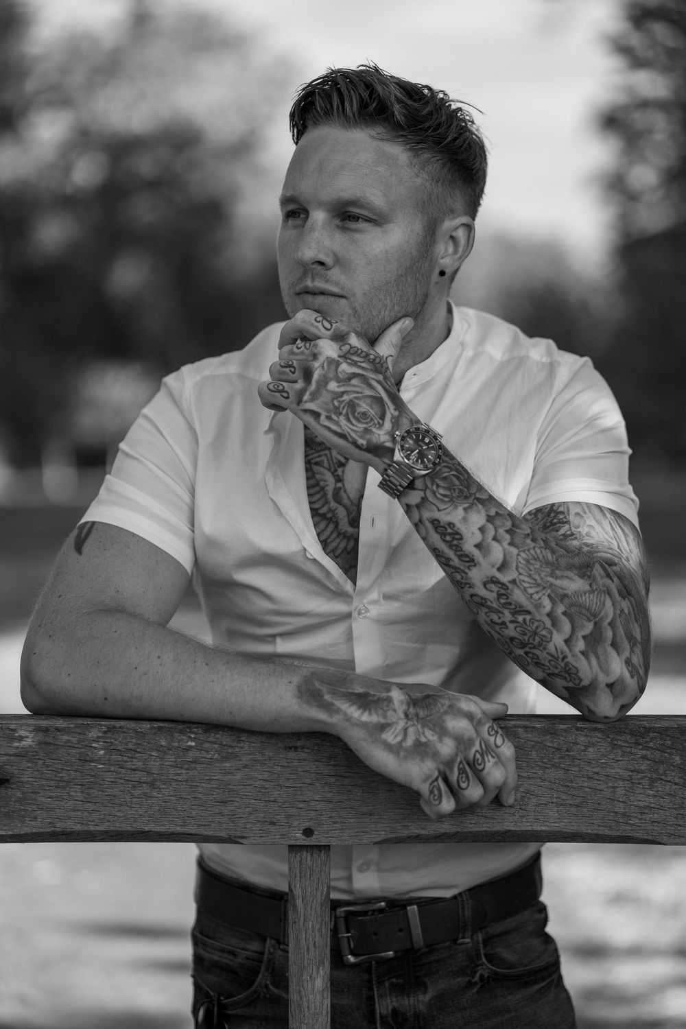 Monochrome portrait showing contemplative pose with detailed tattoo sleeve visible.