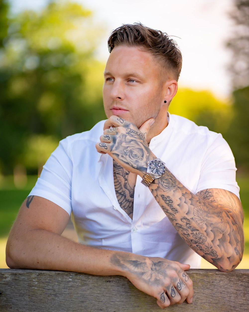 Outdoor portrait featuring white shirt and intricate tattoo artwork in natural lighting.