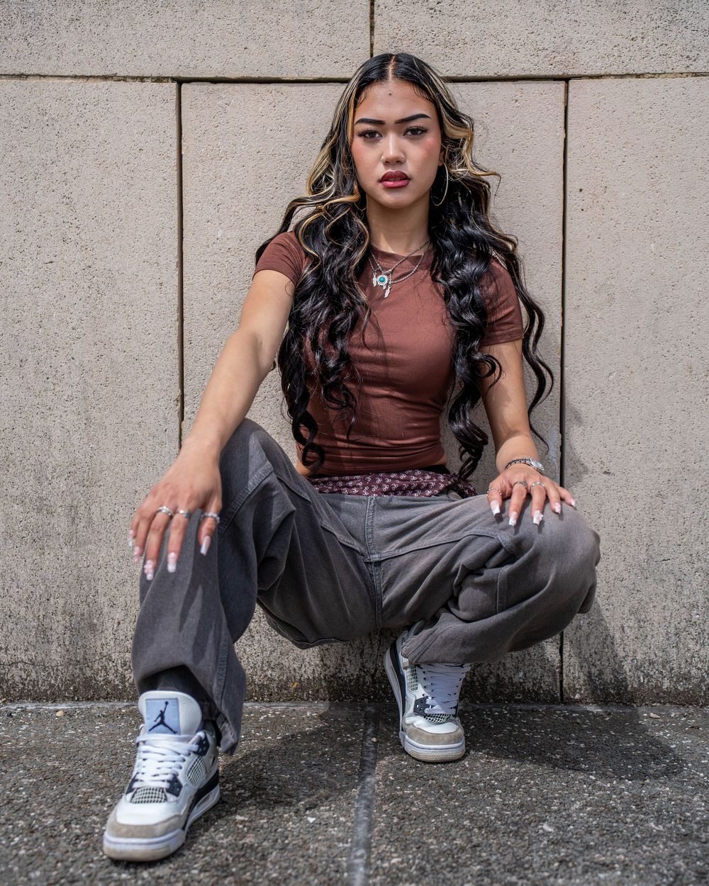 Urban style photo with model in casual wear crouching against concrete wall.