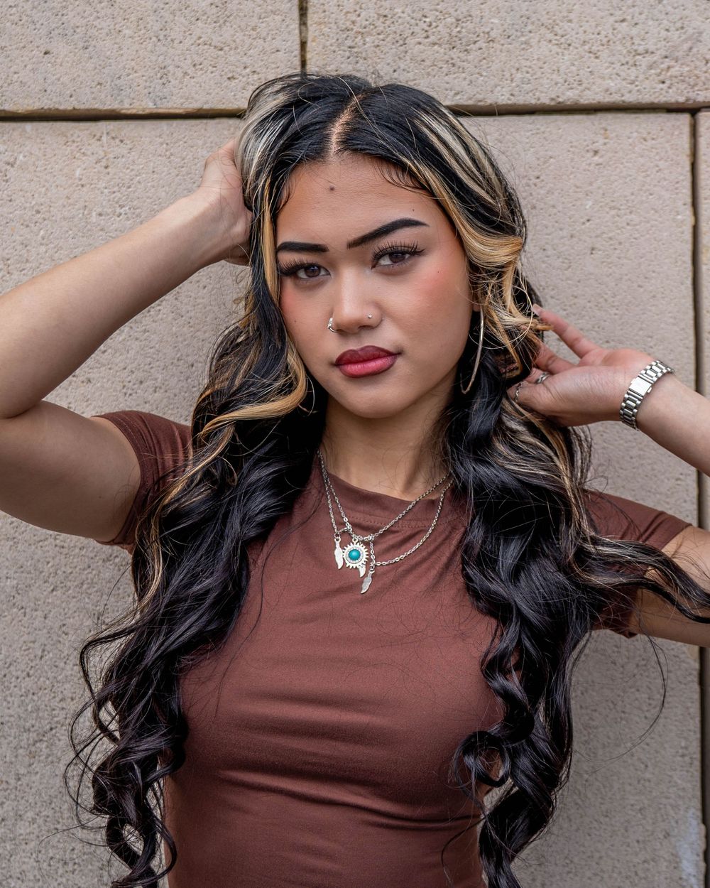 Close-up fashion portrait with wavy highlighted hair and brown fitted top.