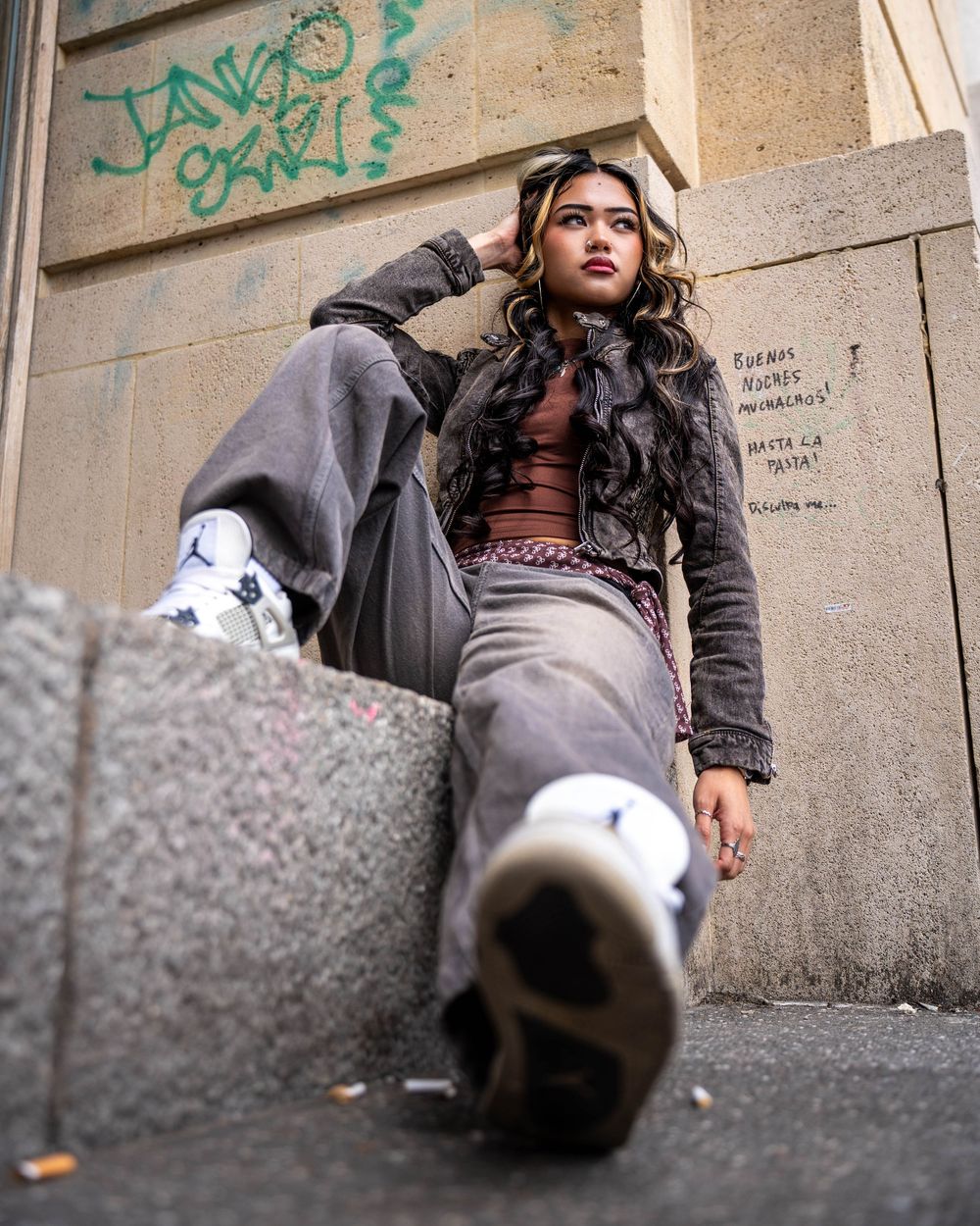 Low angle fashion shot featuring a model in streetwear lounging against a graffiti-covered wall.