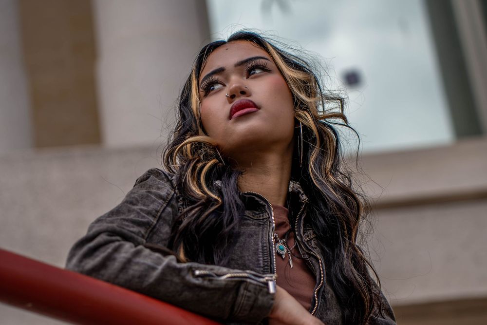 Dramatic upward angle portrait shot showing highlighted hair and red lipstick against an urban backdrop.