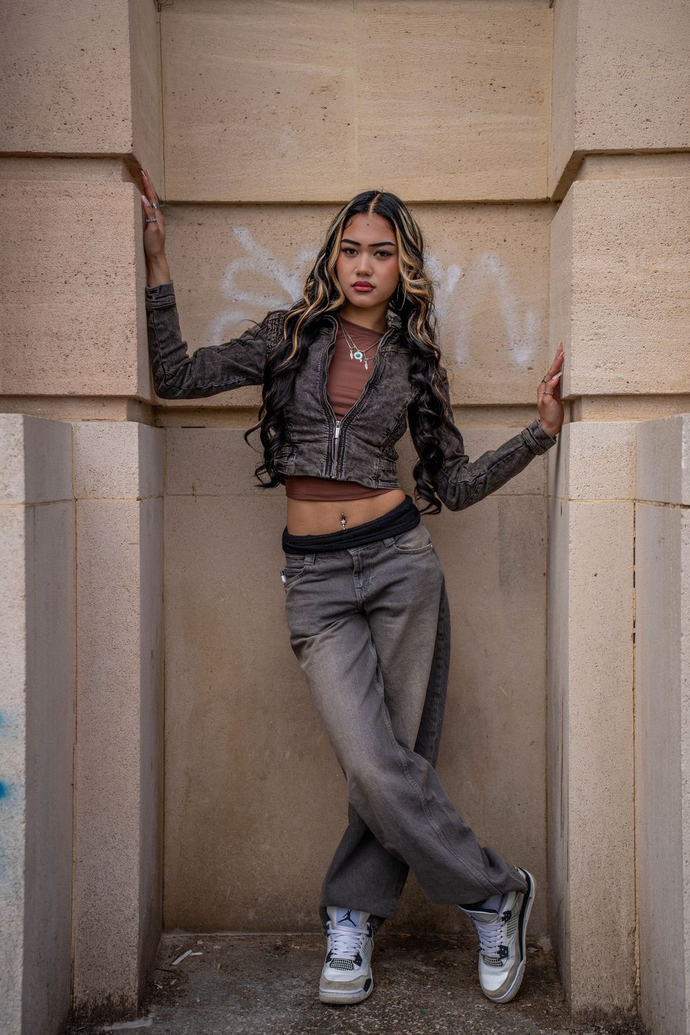 Street style portrait of a model posing in a leather jacket and jeans against a concrete architectural backdrop.
