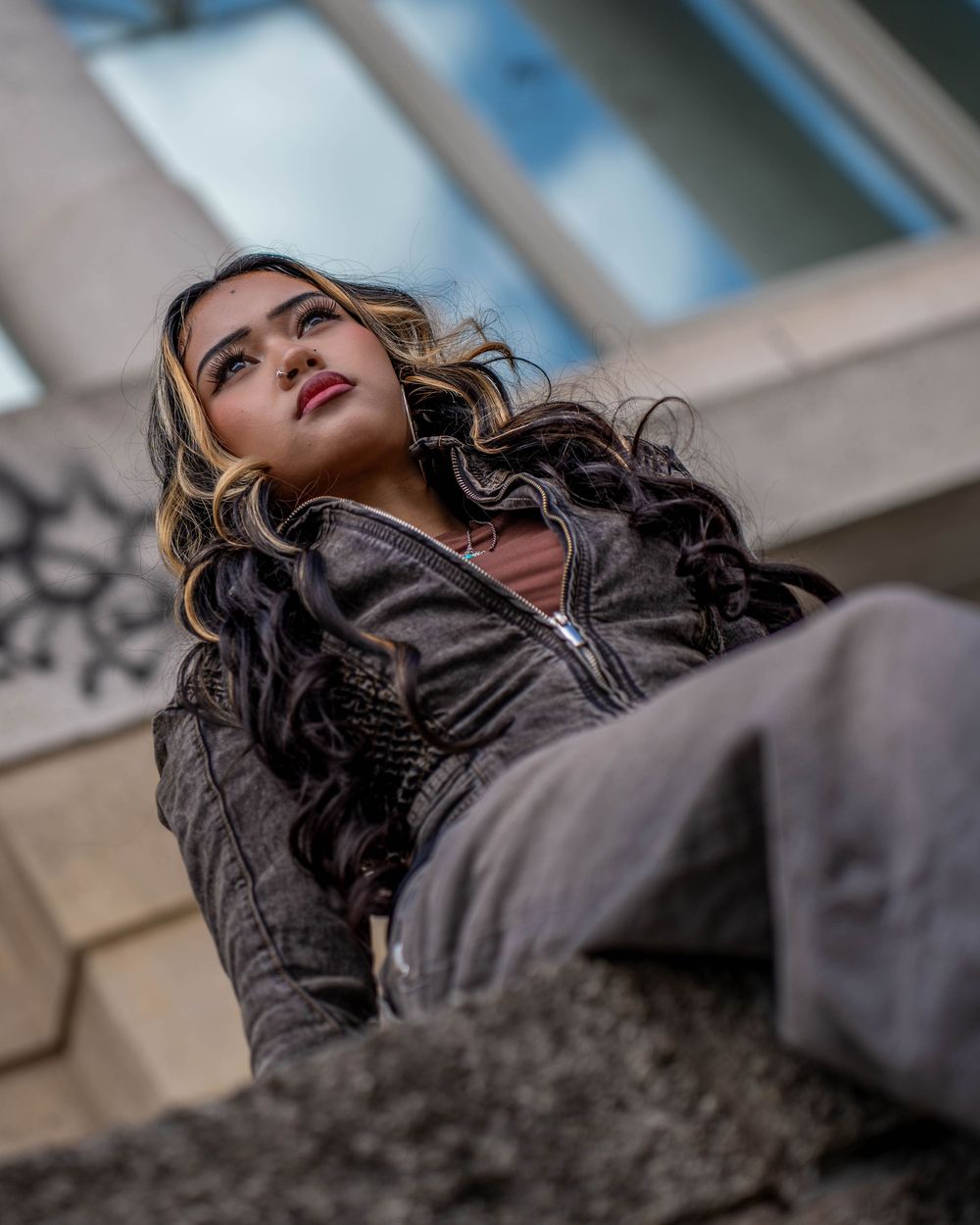 Low angle fashion photography capturing a model in dark leather jacket against architectural elements.
