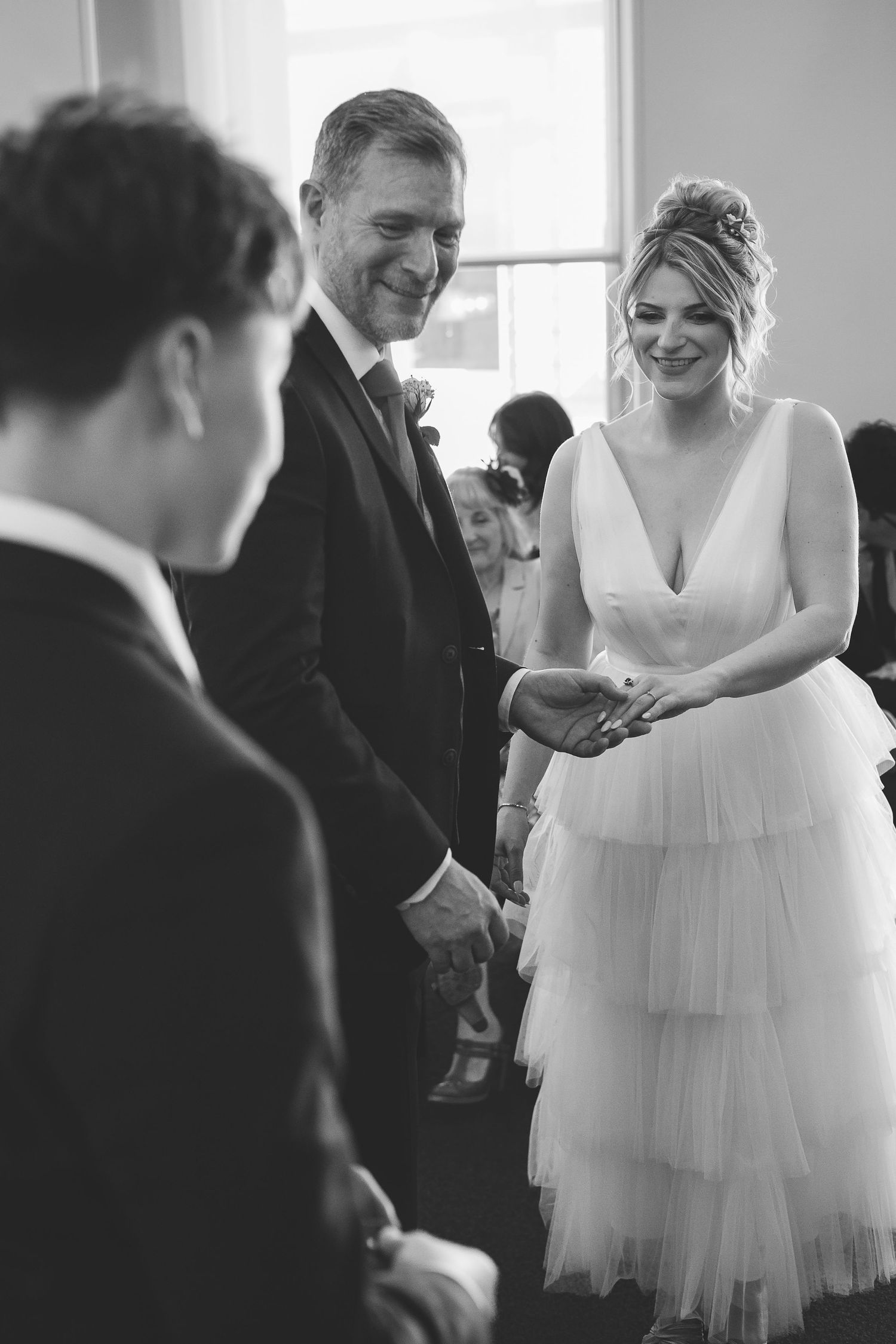 Black and white wedding ceremony photo showing a bride in a tiered tulle dress and groom during the service.