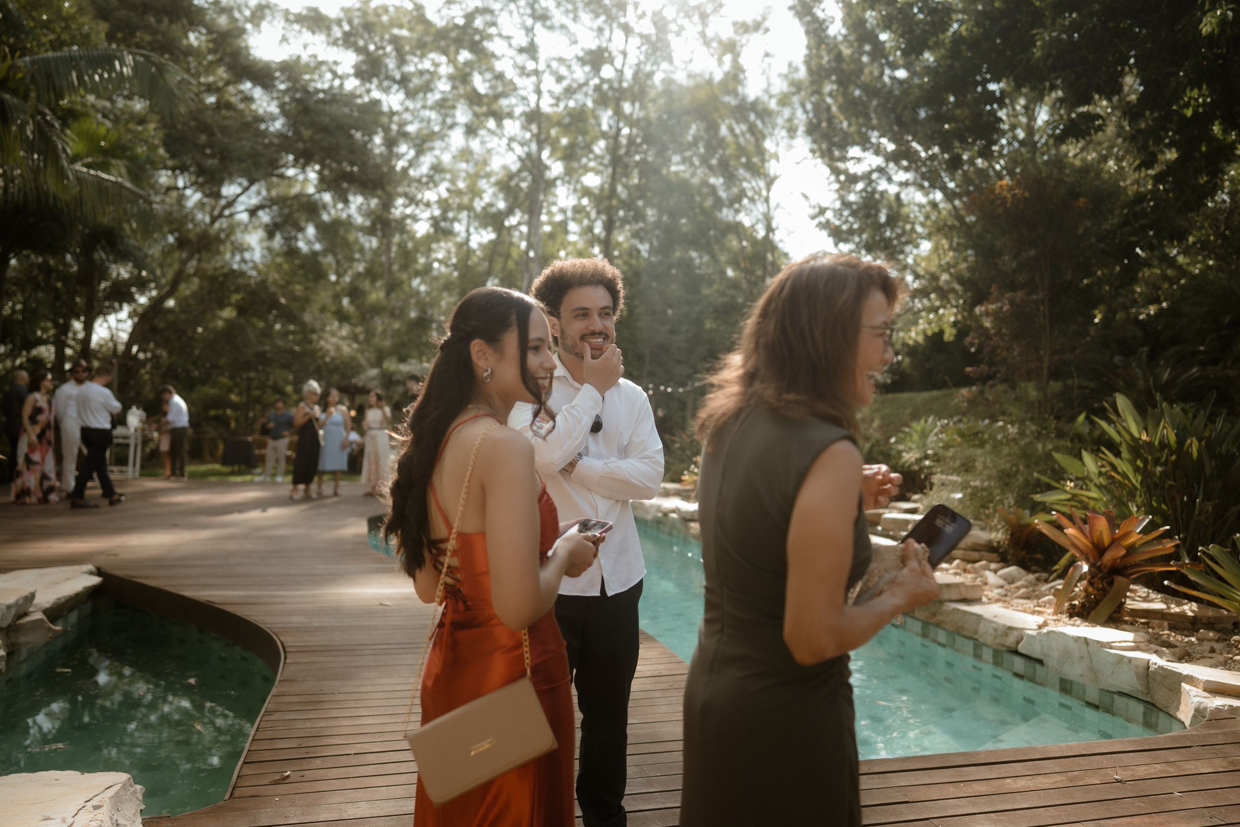 Guests mingling on a wooden deck surrounded by trees during an outdoor event.