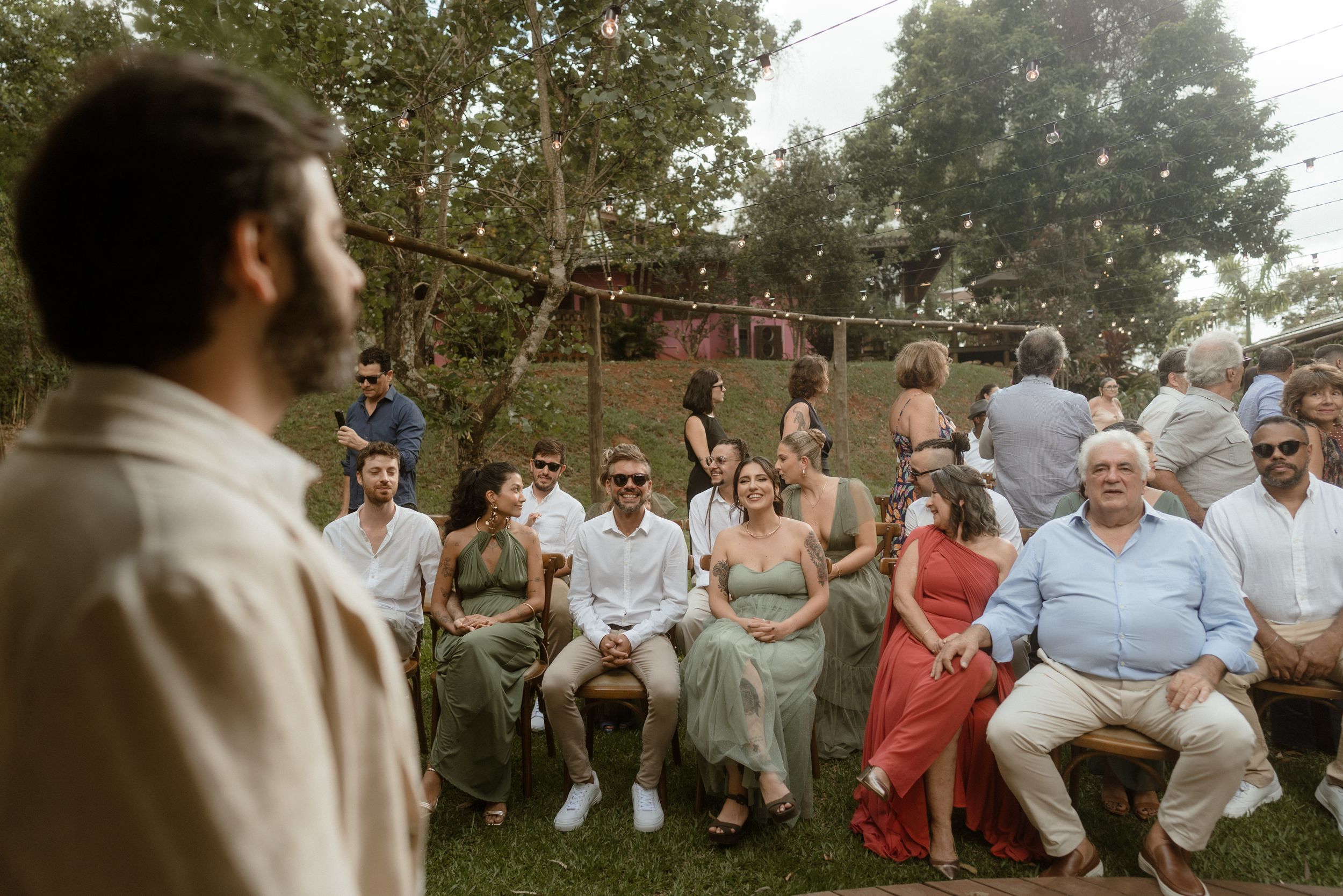 Guests seated outdoors for ceremony with natural wooded backdrop.