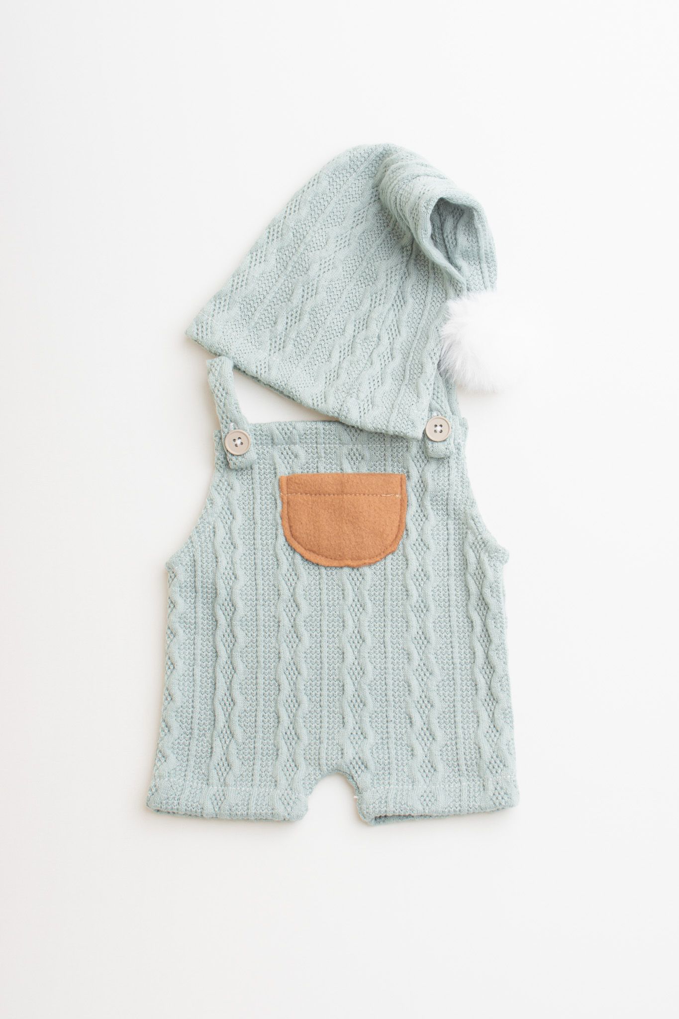 Mint green cable knit baby romper with tan leather pocket and matching knit beanie on white background.