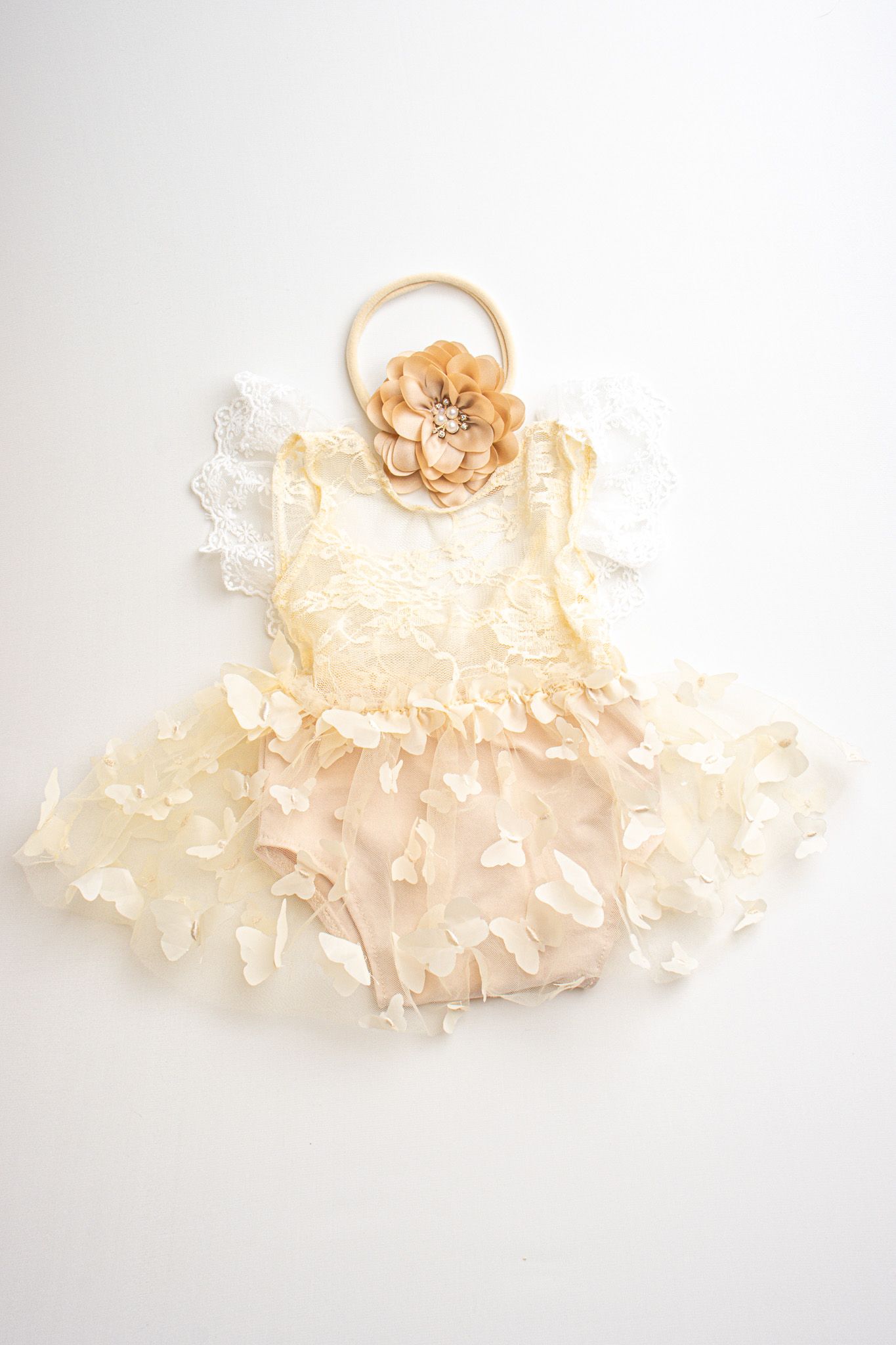 Delicate ivory lace baby dress with ruffled layers and peach flower headband laid flat on white background.