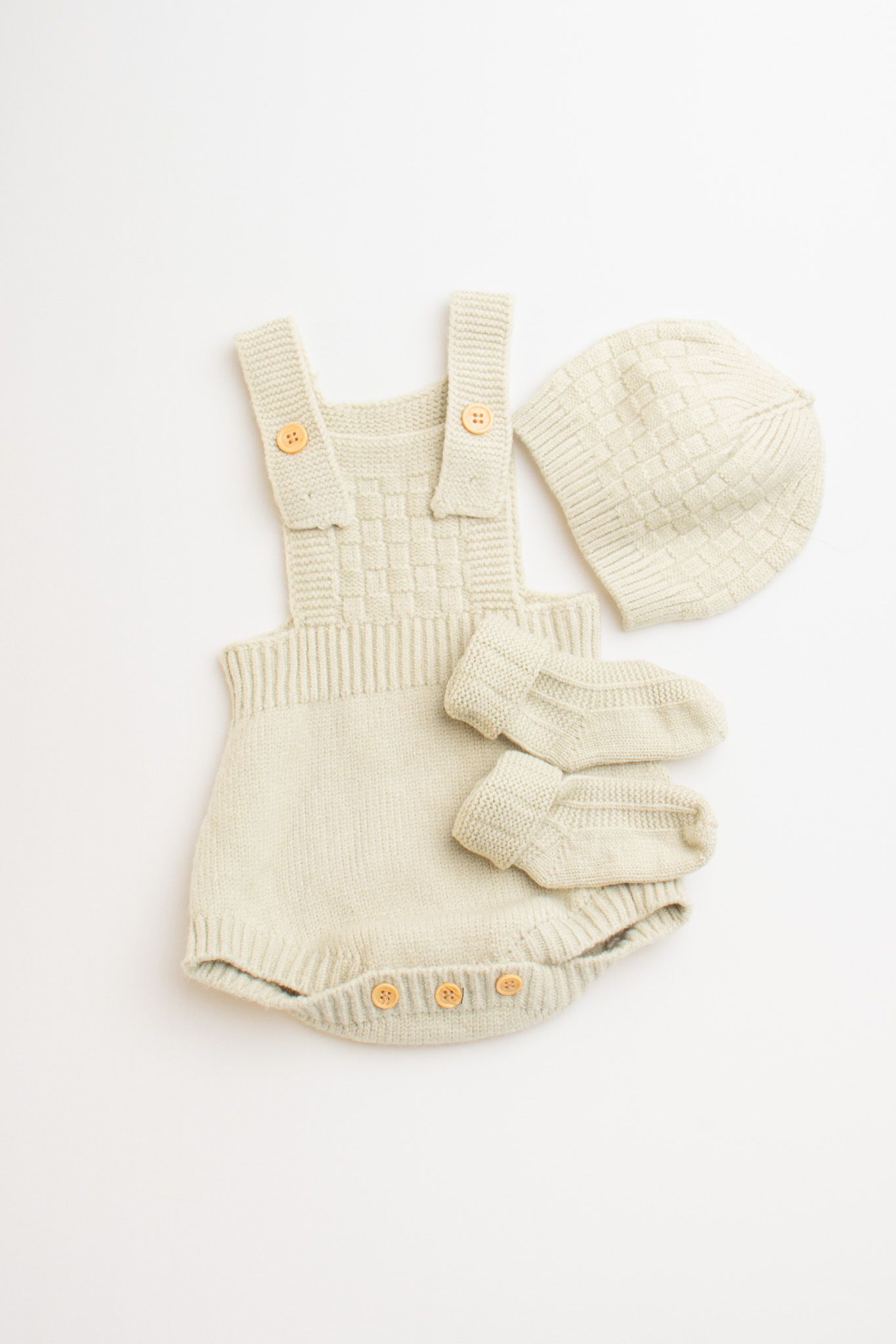 Cream colored knit baby romper with matching hat and socks on white background.
