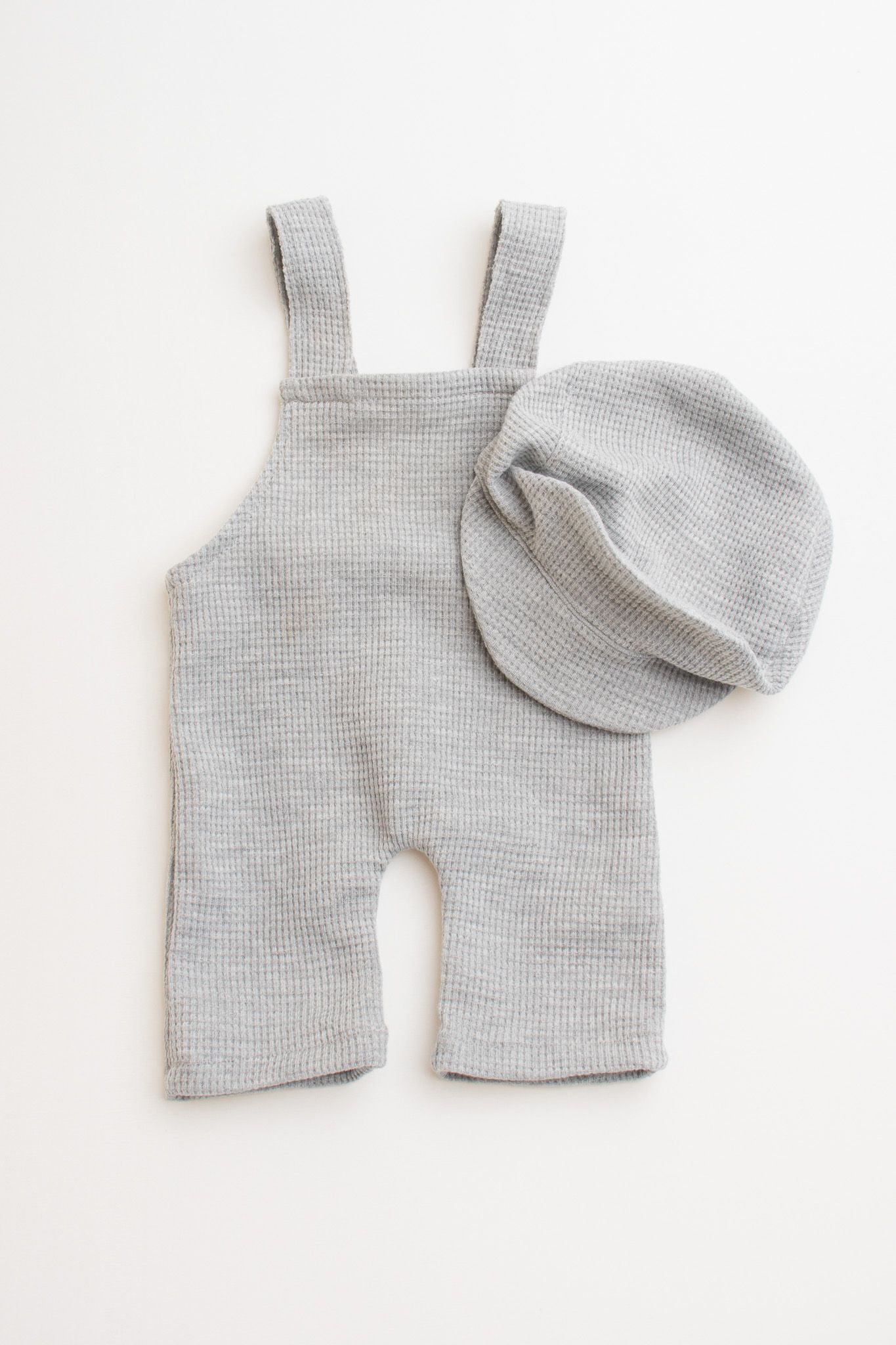 Gray knit baby overalls and matching beanie hat set displayed on white background.