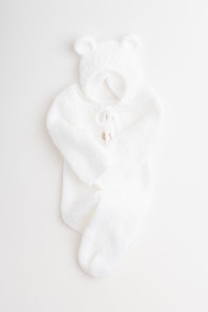 White plush baby onesie with teddy bear ears and buttons lying on a white background.