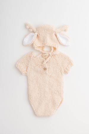 Hand-knitted cream colored baby bodysuit with matching bunny ear hat featuring delicate knit pattern and buttons.