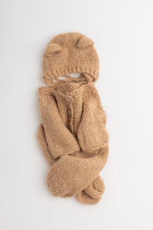 Cozy knit baby outfit in beige color with hat, sweater, and booties laid flat on white background.