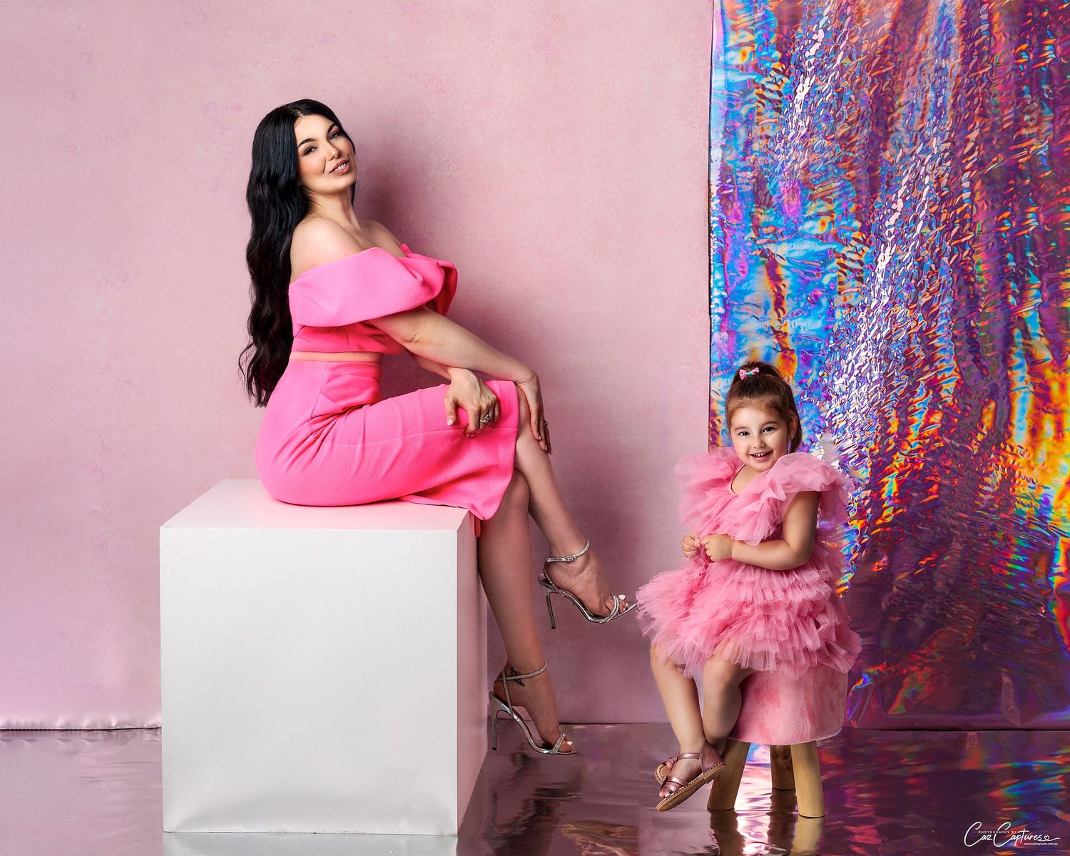 Matching mother and daughter in pink dresses, against pink hand painted canvas smiling