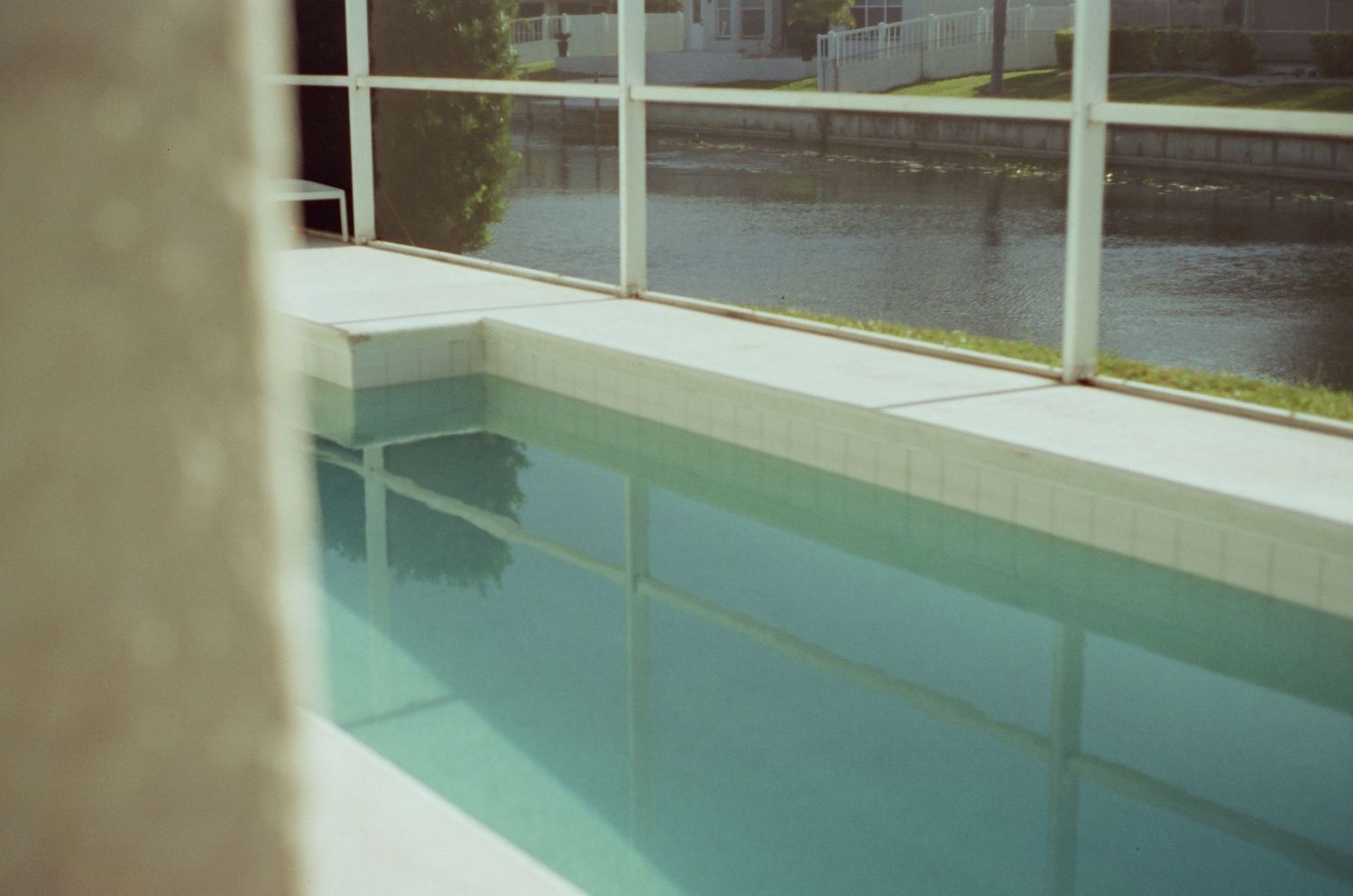 View through glass window showing an indoor swimming pool with turquoise water and white tiled edges.