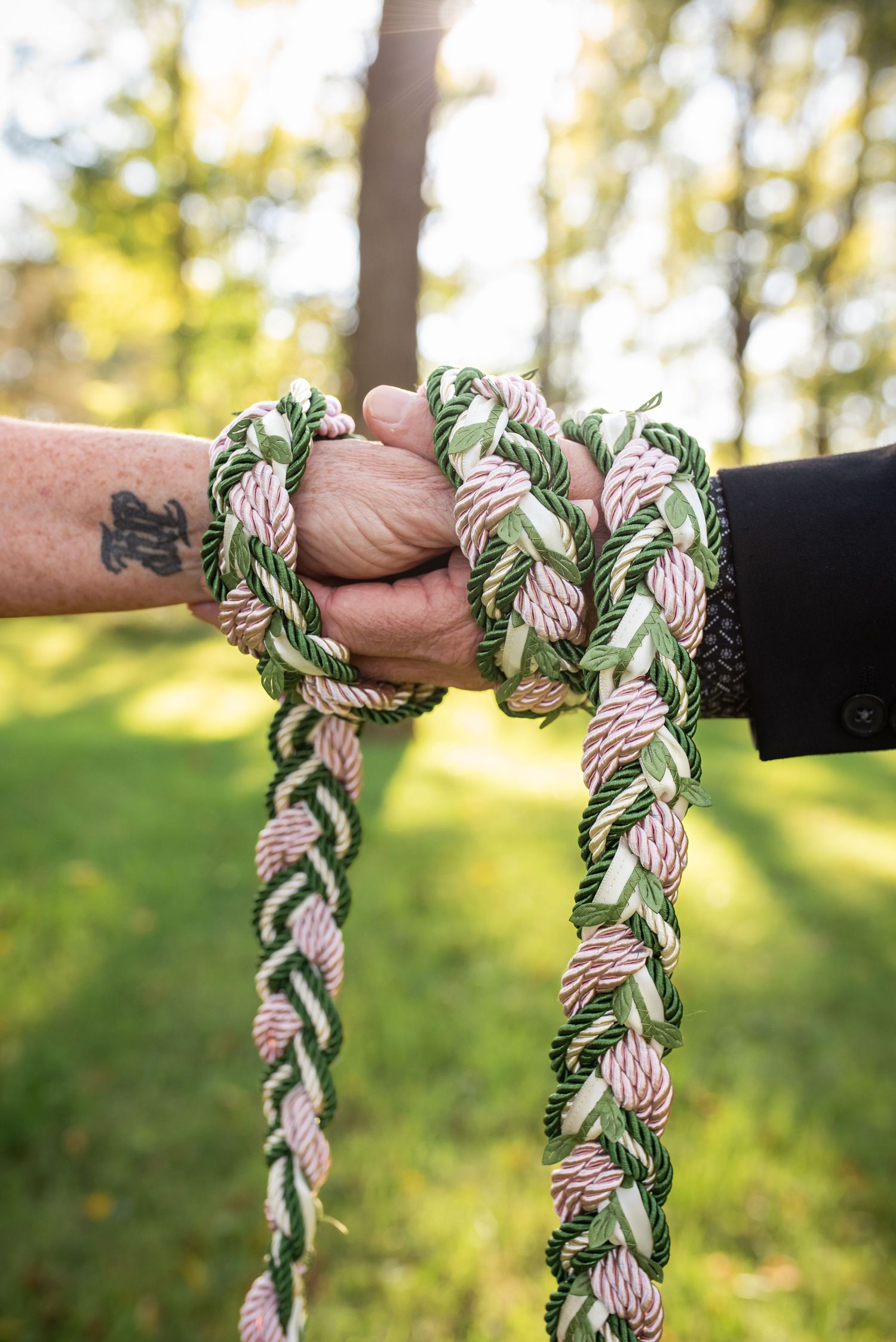 Close-up of hands holding braided ceremonial cords in outdoor setting.