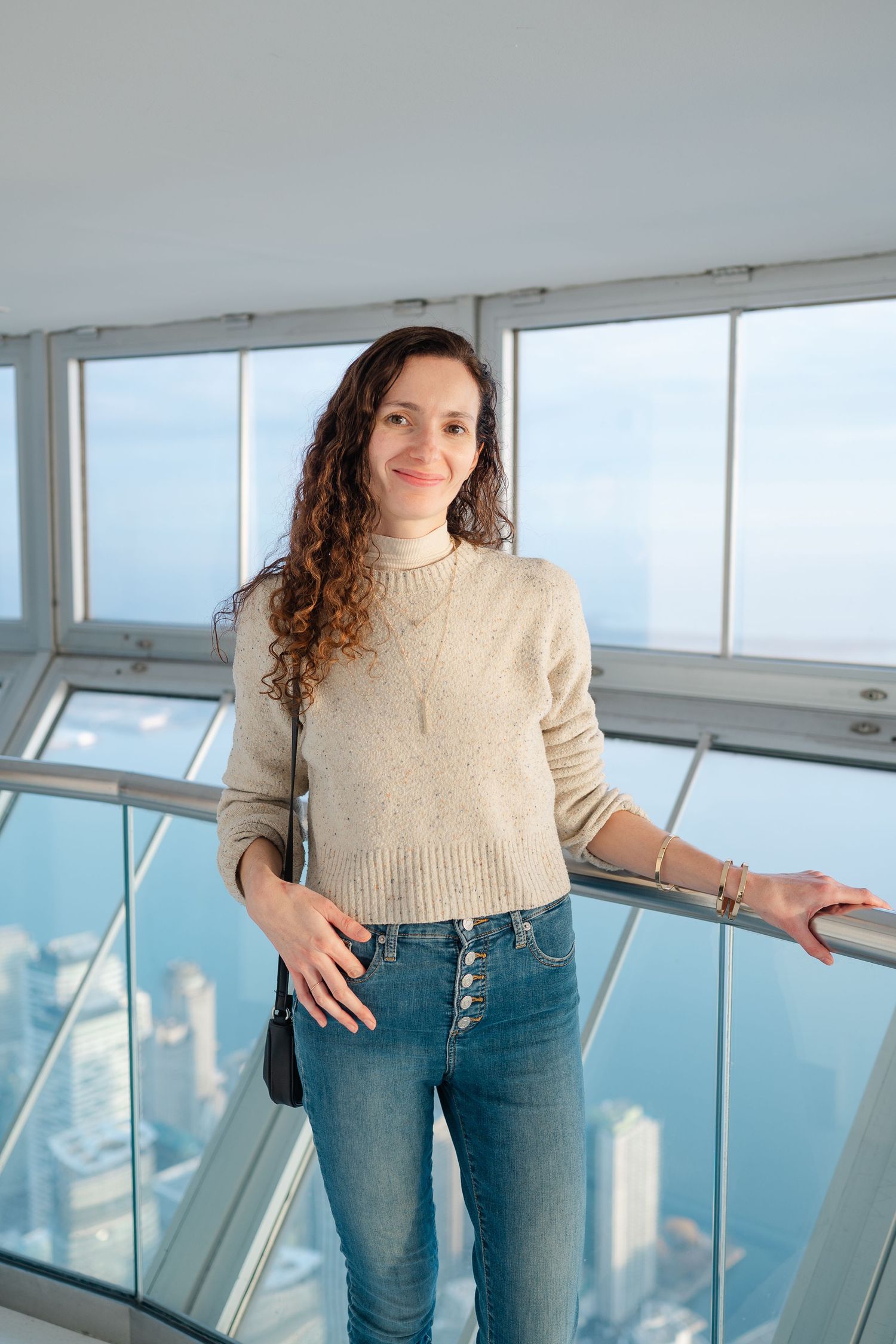 Professional photographer in white sweater and jeans holding camera outdoors in sunlit natural setting.