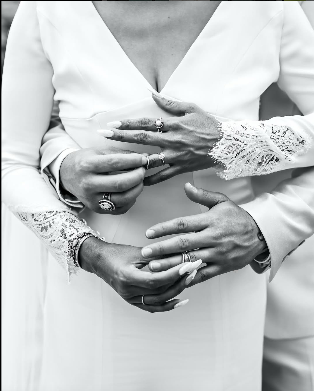 Close-up black and white detail of hands with rings and lace wedding attire.