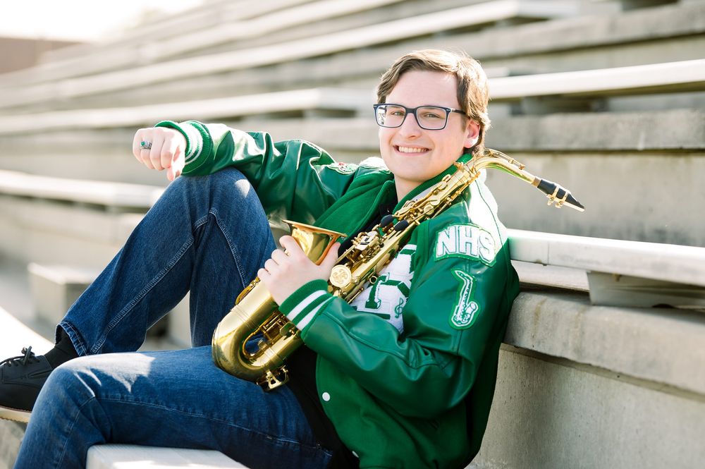 Band student relaxes on stadium bleachers with saxophone in casual pose.