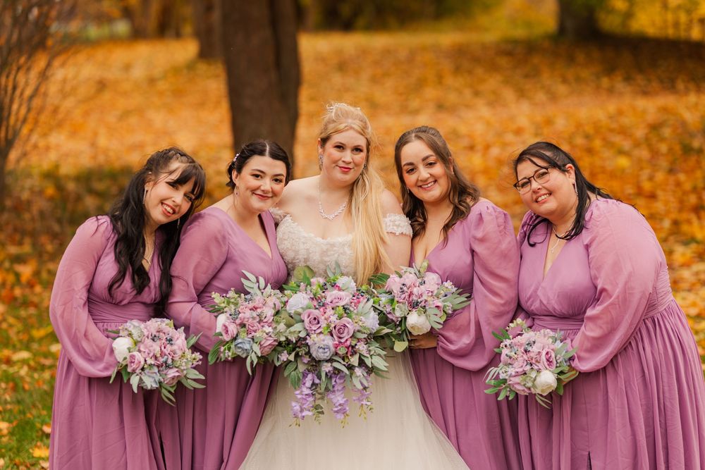 Wedding party in mauve dresses poses together among vibrant autumn foliage.